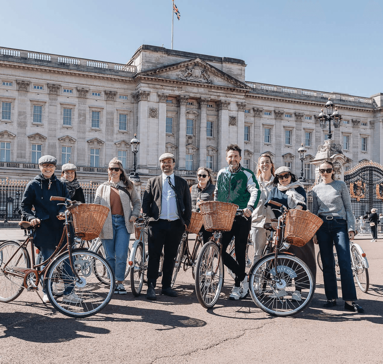 Group of guests standing with vintage-style bicycles equipped with wicker baskets outside Buckingham Palace during our guided London bike tour